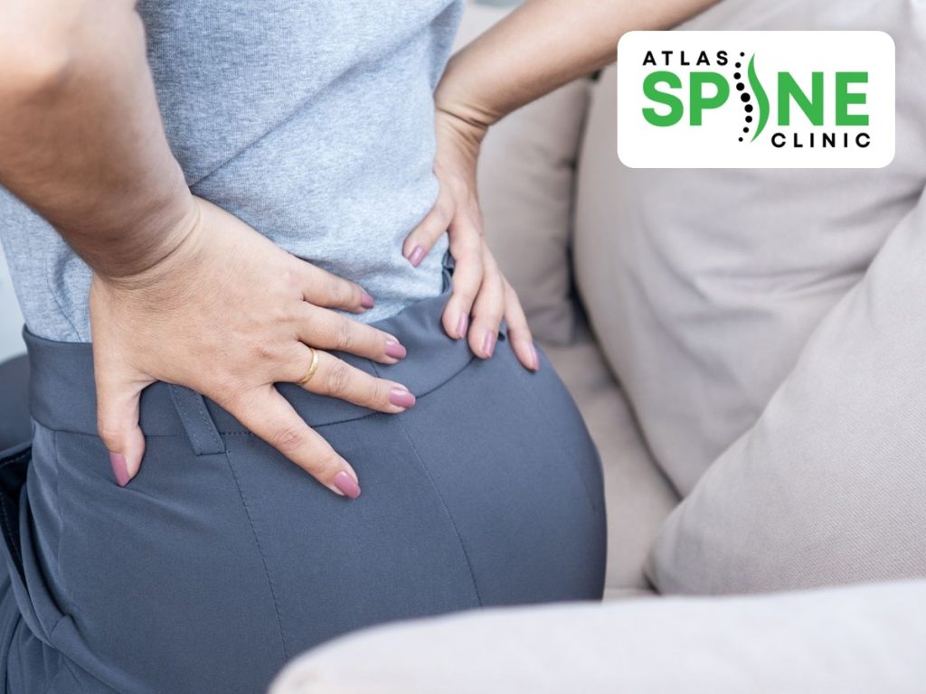 Person sitting on a sofa holding one side of the low back and buttock in pain